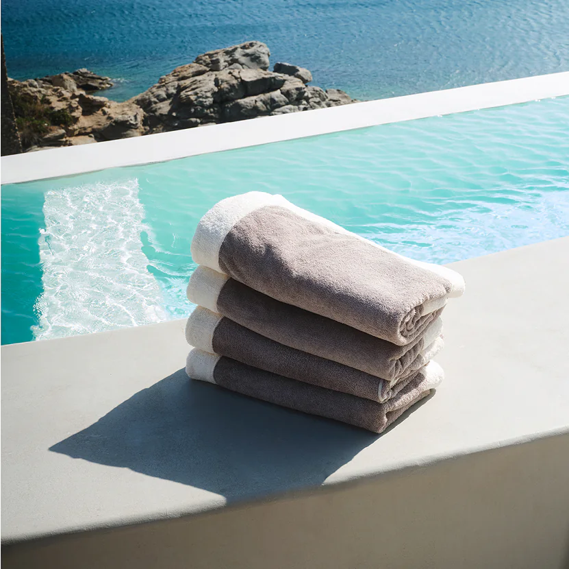 Stack of luxury hotel beach towels placed by an infinity pool overlooking the sea, designed for premium hospitality and resort comfort.