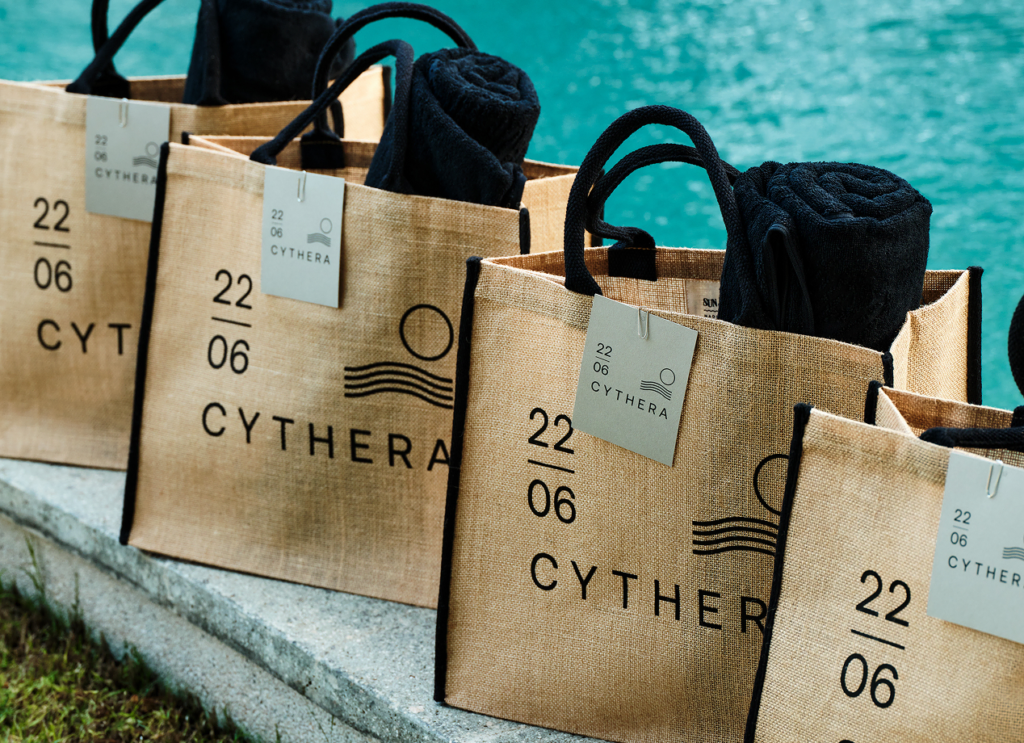 Stylish and sustainable branded tote bags featuring elegant black handles are beautifully arranged by the poolside, each one holding luxurious pool towels.