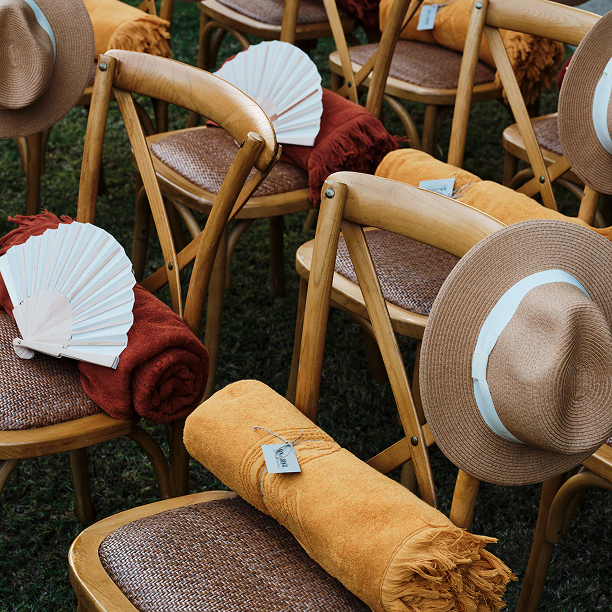 Wedding chairs with hats and burgundy and yellow towels for guests, perfect for social event gifting.