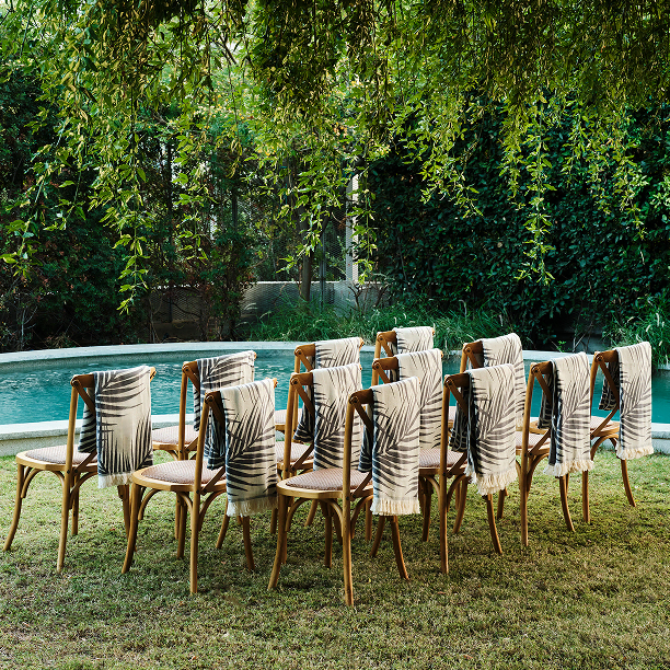 Wooden chairs by the pool with towels hanging, set up for a wedding, ideal for social event gifting.