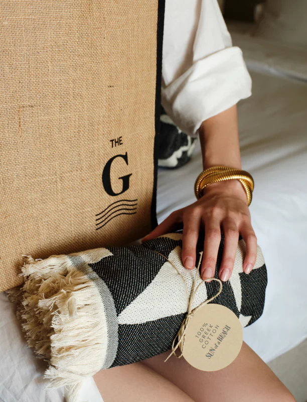 A woman unpacking a beach towel from a gift bag, part of a curated Sun of a Beach welcome gift for hotel guests.